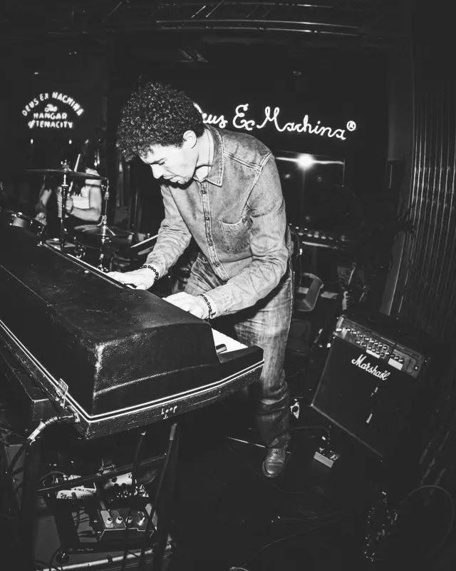 Claviériste penché sur son clavier sous l'enseigne du Deus Ex Machina, photo noir et blanc