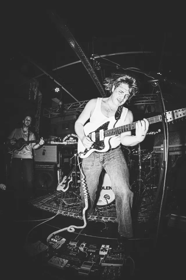 Guitariste en débardeur blanc sur scène, photo noir et blanc